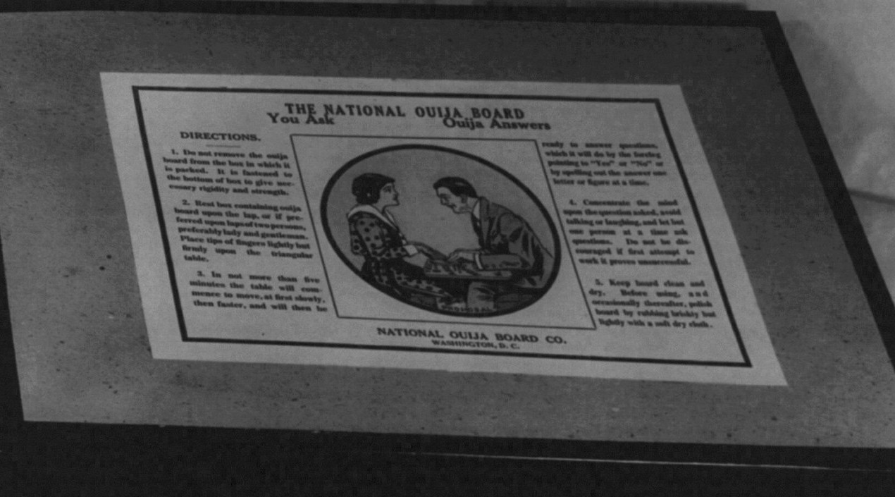 A 1920 photograph of a National Ouija Board box, its printed DIRECTIONS facing the camera, instructing the user to place the tips of their fingers lightly but firmly upon the triangular table and wait for it to move.